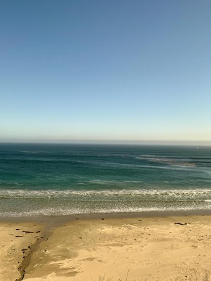 dark blue green ocean with some white foam waves at the front rolling up on the yellow sand.