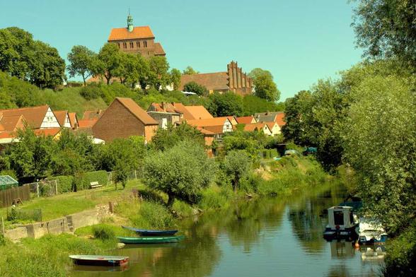 Doie Havel mit kleinen Booten, am Ufer Bäume, Wiesen und Fachwerkhäuser. Auf einem Hügel der Westbau des Havelberger Doms.