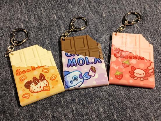 Keychains of a white chocolate sea bunny, milk chocolate mola, and strawberry chocolate axolotl.