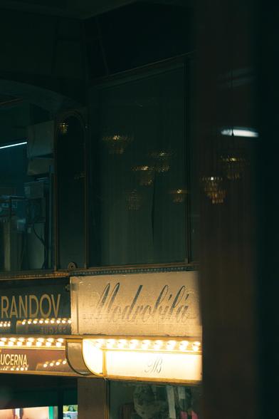A photo showing czech shop signage taken through a café window at night. In the window reflection ghostly chandeliers are seen. Taken in Prague, Czechia