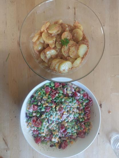 Zwei Schüsseln. In einer sind Kartoffelscheiben in einer braunen Sauce mit veganen Speckwürfeln und in der anderen verschiedene Hülsenfrüchte in Joghurtsauce