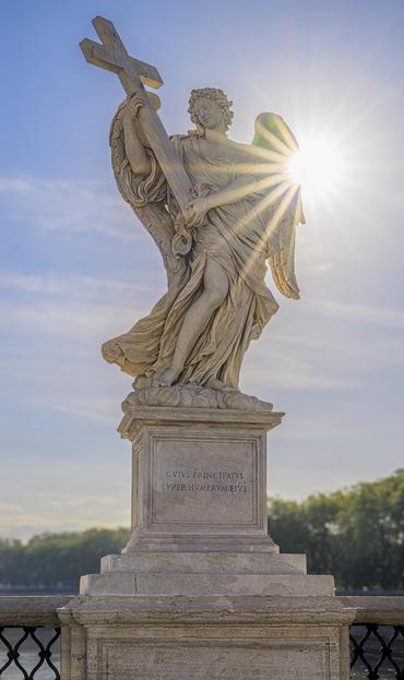 A Statue of an angel carrying a cross with a sunstar on the right of the statue, found on the Ponte Sant'Angelo in Rome.