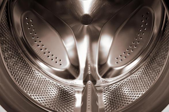 The image is of the interior of a washing machine drum. The metallic surface and perforations for water drainage are visible.