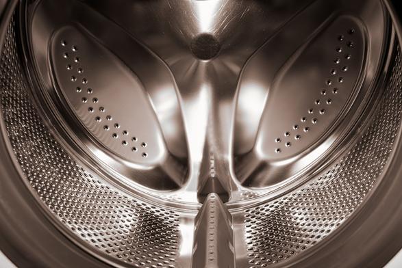 The image is of the interior of a washing machine drum. The metallic surface and perforations for water drainage are visible.