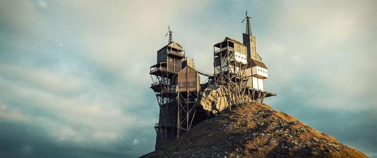 Wide shot, exterior, day -

A series of wood and plaster buildings, constructed at the top of a hill with a large boulder on top. Everything is chaotic, with buildings, pillars and platforms combining with seemingly no plan or organization. Two wind turbines are built at the top of the two largest structures.