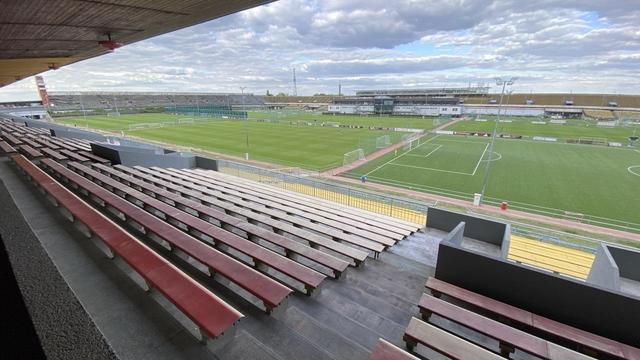 Ein sehr großes Sportstadion von innen. Leere Zuschauerränge und das Sportfeld mit insgesamt 8 Fußballfeldern.