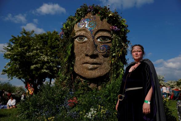 A  poses next to a statue (a stone head adorned with leaves) at the #Bealtaine fire festival.
