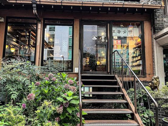 A charming shopfront with stairs surrounded by greenery and flowers.