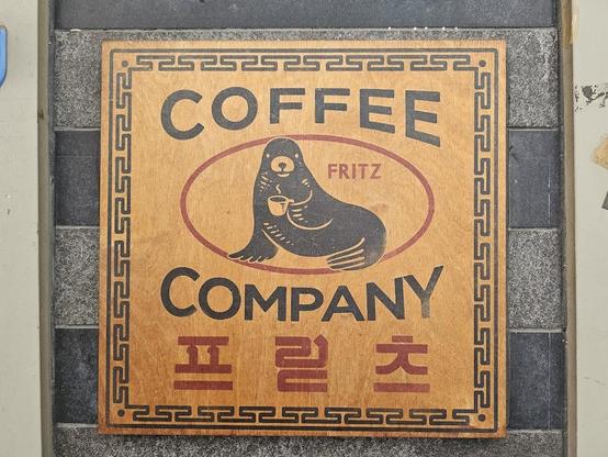 A sign for Fritz Coffee Company featuring a seal holding a coffee cup, framed by a geometric border.