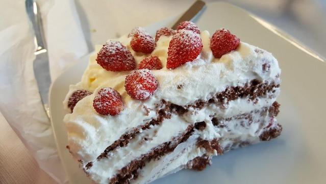 A slice of chocolate cake is covered in whipped cream and strawberries, dusted with powdered sugar.