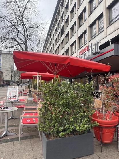 Outdoor seating area with red umbrellas and plants in front of Cafe Extrablatt.