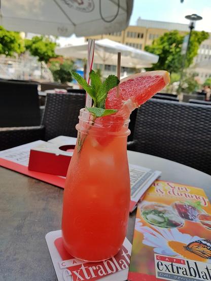 A refreshing grapefruit cocktail with mint garnish, served outdoors at a cafe.