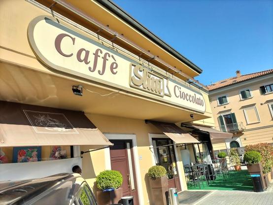 "Caffè Slitti Cioccolato" is visible on a tan building with awnings. Outdoor seating is present, and a building is in the background.