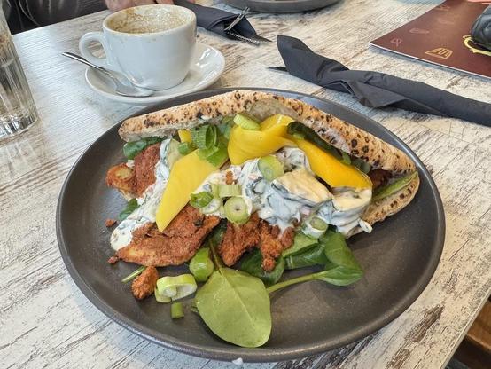 A flatbread sandwich with chicken, greens, mango, and a creamy sauce on a dark plate.