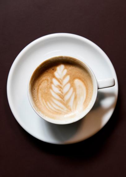 A latte with latte art on a white saucer, set against a dark brown background.