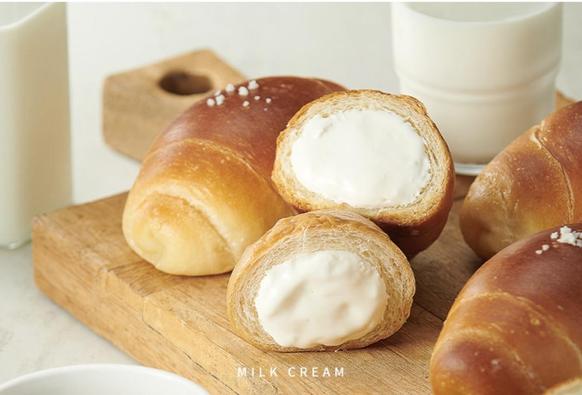 An eye-level close-up shows cream-filled pastries on a wooden board next to glasses of milk.