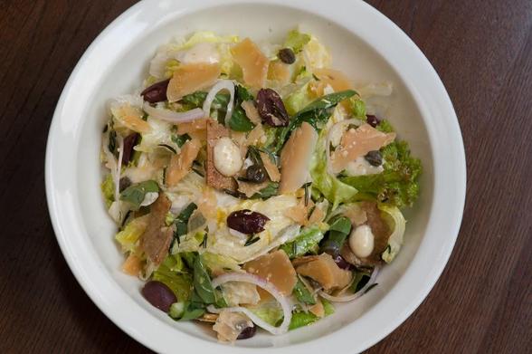 Overhead shot of a salad with lettuce, cheese, olives, and croutons in a white bowl.