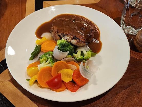 A plated meal with a sauced meat portion and colorful steamed vegetables.