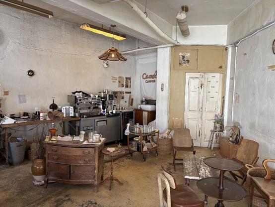 The image showcases a vintage-style café interior with a rustic charm. A coffee preparation area, various tables, and an eclectic mix of chairs give the space a warm and inviting atmosphere.