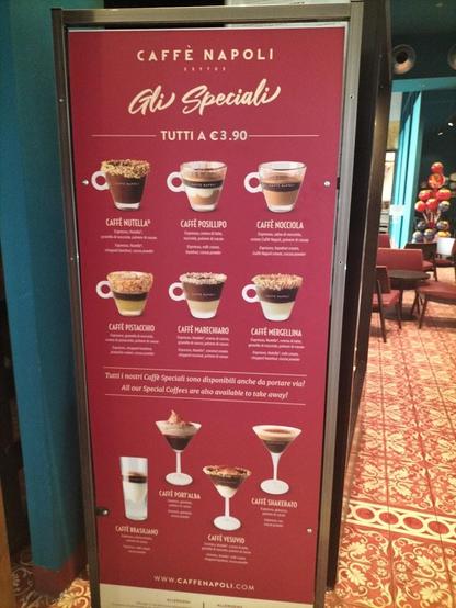 A close-up shot of a menu board advertising various coffee drinks from Caffè Napoli, featuring names, descriptions, and prices of the drinks.