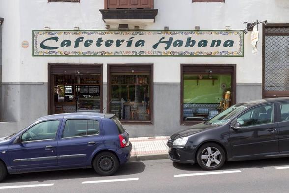 A cafe called "Cafeteria Habana" with two cars parked in front.