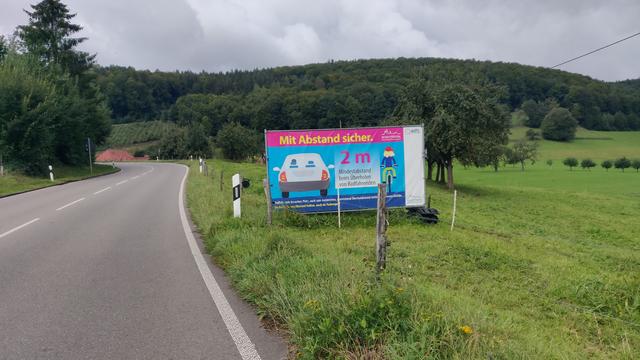 Banner einer Campagne zum Überholabstand. "Mit Abstand sicher. 2 m" in der Weide an einer Schwarzwaldstraße. Banner einer Campagne zum Überholabstand. "Mit Abstand sicher. 2 m" in der Weide an einer Schwarzwaldstraße.
