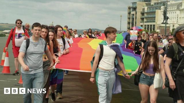 A group of people holding a rainbow flag on Plymouth Hoe