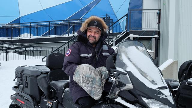 Un homme souriant sur un motoneige, dans un paysage enneigé.