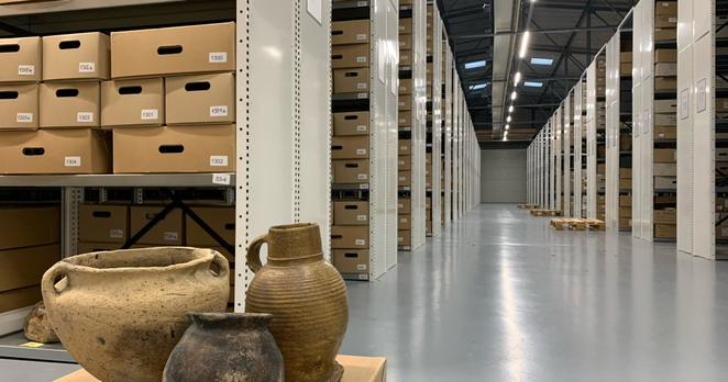 Een paar oude kannen en kruiken staan op een doos in het midden van een grote opslagloods.