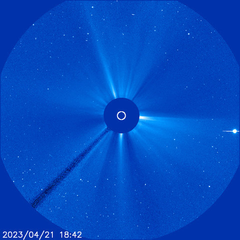 A circular, blue-colored view shows stars around the Sun, which is covered by a dark blue disk at the center. A small white circle in the center of the disk shows the size of the Sun. Streams of material extend away from the disk, and then a white halo of material erupts and moves away from the disk in all directions. A bright dot appears on the right.