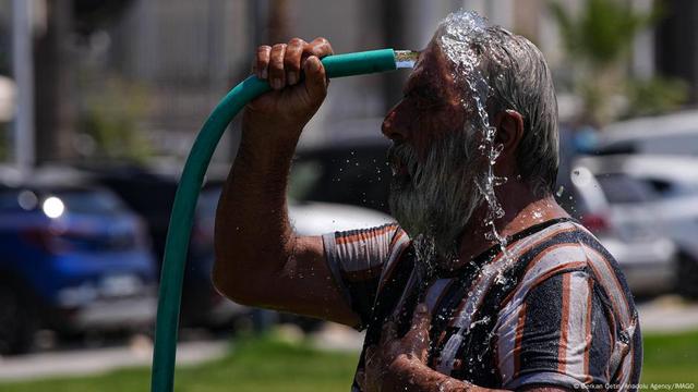 A man washes his head with a garden hose to cool down as Turkey is hit by a heat wave.