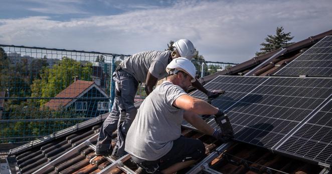 Zwei Männer installieren auf einem Hausdach eine Photovoltaik-Anlage