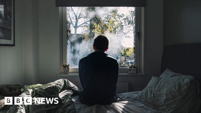 An anonymous man sitting on a bed looking out of the window
