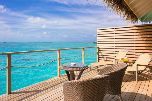 A tropical scene of chairs on a wooden deck in the Maldives overlooking clear blue water under a partly cloudy sky