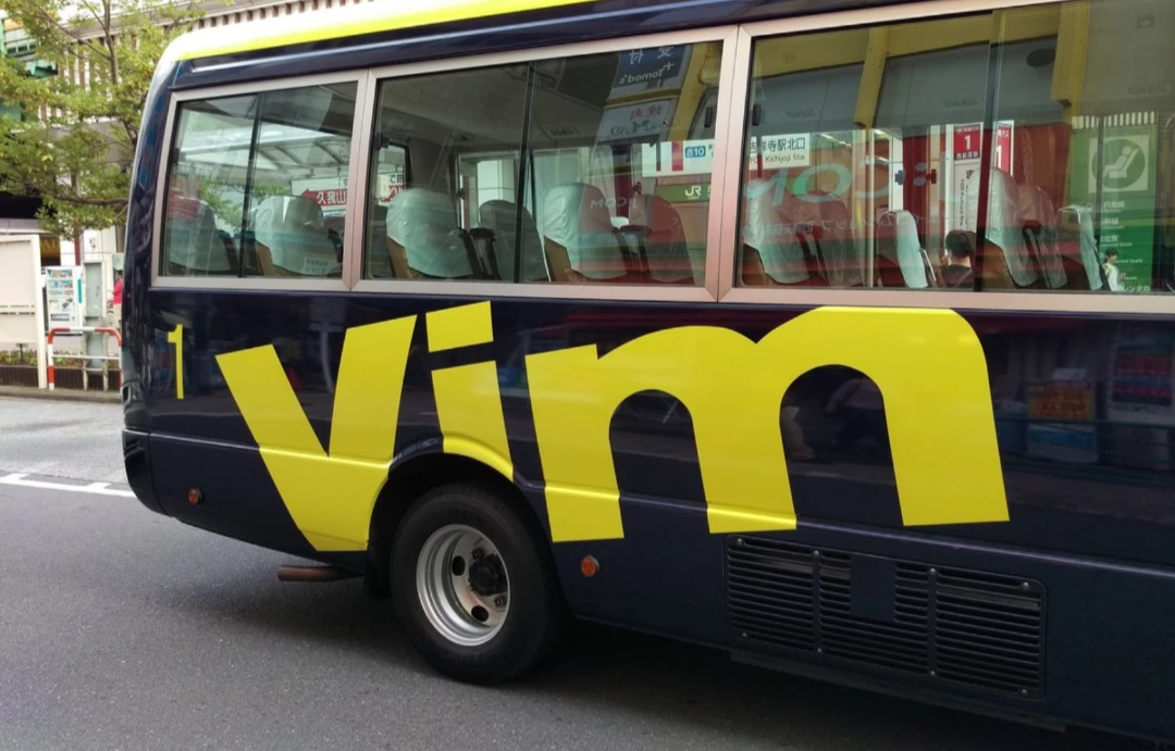 A black bus in a street with the word "Vim" on the side in yellow letters above the rear wheel.