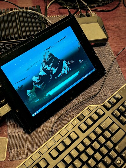 Keyboard in foreground and bare display showing Manjaro KDE desktop in midground. Pi in Argon case in back right. Another headless unit (new firewall) is supporting the display.