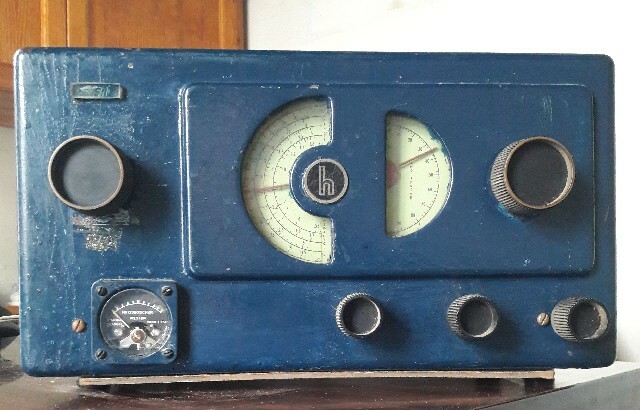 An old short wave radio, Hallicrafters S-38, painted blue. Tuning dials, coarse (left) and fine (righy) are half vertival circles at the center of the faceplate.