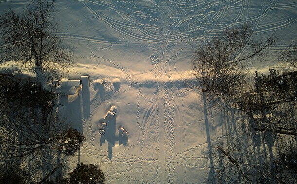 Drone photo looking directly down on the shoreline of a snowcovered lake. 

The snow is covered with animal tracks and signs of human activity. Scattered yard items are covered in snow.