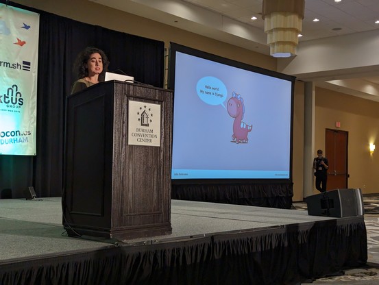 Julia at the podium with a slide featuring a pink cartoon pony with a speech bubble that says "Hello world. My name is Django."