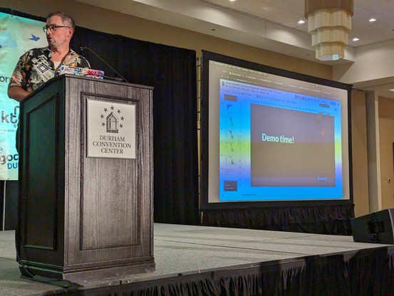 Thibaud at the podium next to a slide with "Demo Time!" 