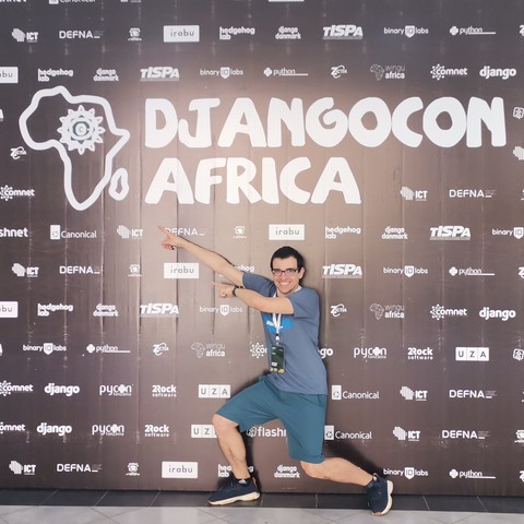 Me in front of the DjangoCon Africa wall with its logo and smaller sponsor logos
