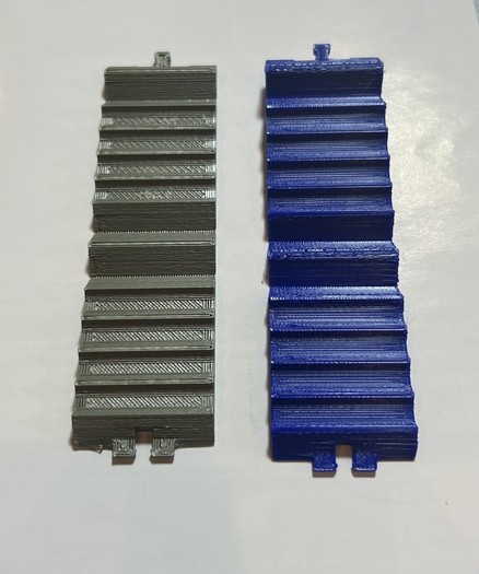 Two 3D printed parts, one grey/gold and the other blue on a white background. They are kind of ridged and rectangular but other wise mysterious 