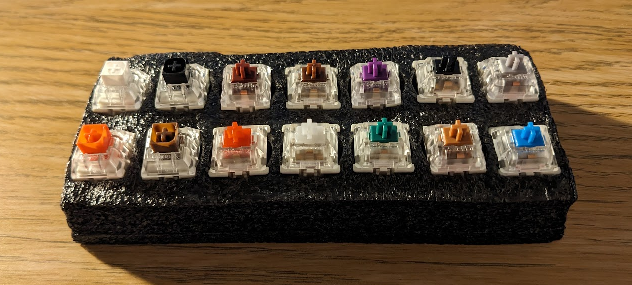 A photo of a sample set of mechanical keyboard switches on a desk. The switches are in black foam, and from a distance looks a bit like sushi