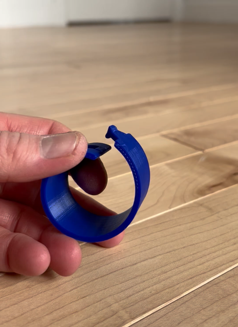Hands manipulating a blue 3d printed spiral that latches together. Background is a wood floor.
