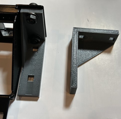 On the right: A grey bracket mounted in a black patch panel.

On the left: a mirror copy of the bracket unattached to the panel.

Everything is on a white background 