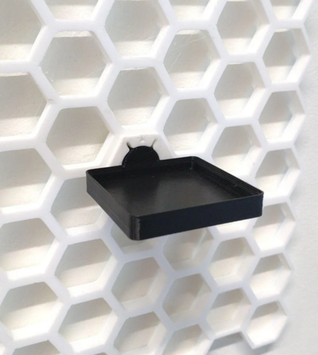honeycomb storage wall with a white screwiverse threaded insert and a black 1x1 gridfinity plate screwed in