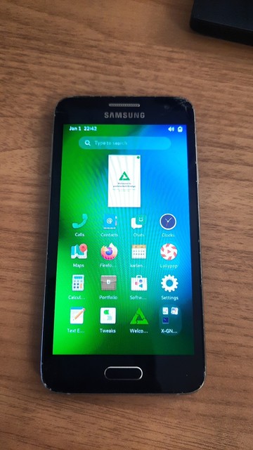 Picture of a Samsung Galaxy A3 on my desk, running postmarketOS with GNOME mobile shell.