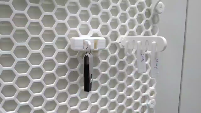 video, showing honeycomb storage wall. a hand grabs a USB stick which is attached to a small white box. The USB stick can't be removed from the box. The hand then grabs a name tag labeled 'Bob' from the right, inserts it into a slot on the box, and the USB stick pops out. Now the name tag can't be removed from the box. In reverse, when reinserting the USB stick, the name tag pops out.
