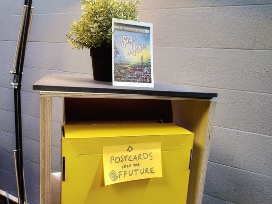 A yellow box for postcards from the future, with sci fi art and a small plant