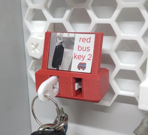 red 3d printed keyguardian with lavel holder, holding a key for a minivan on a honeycomb storage wall